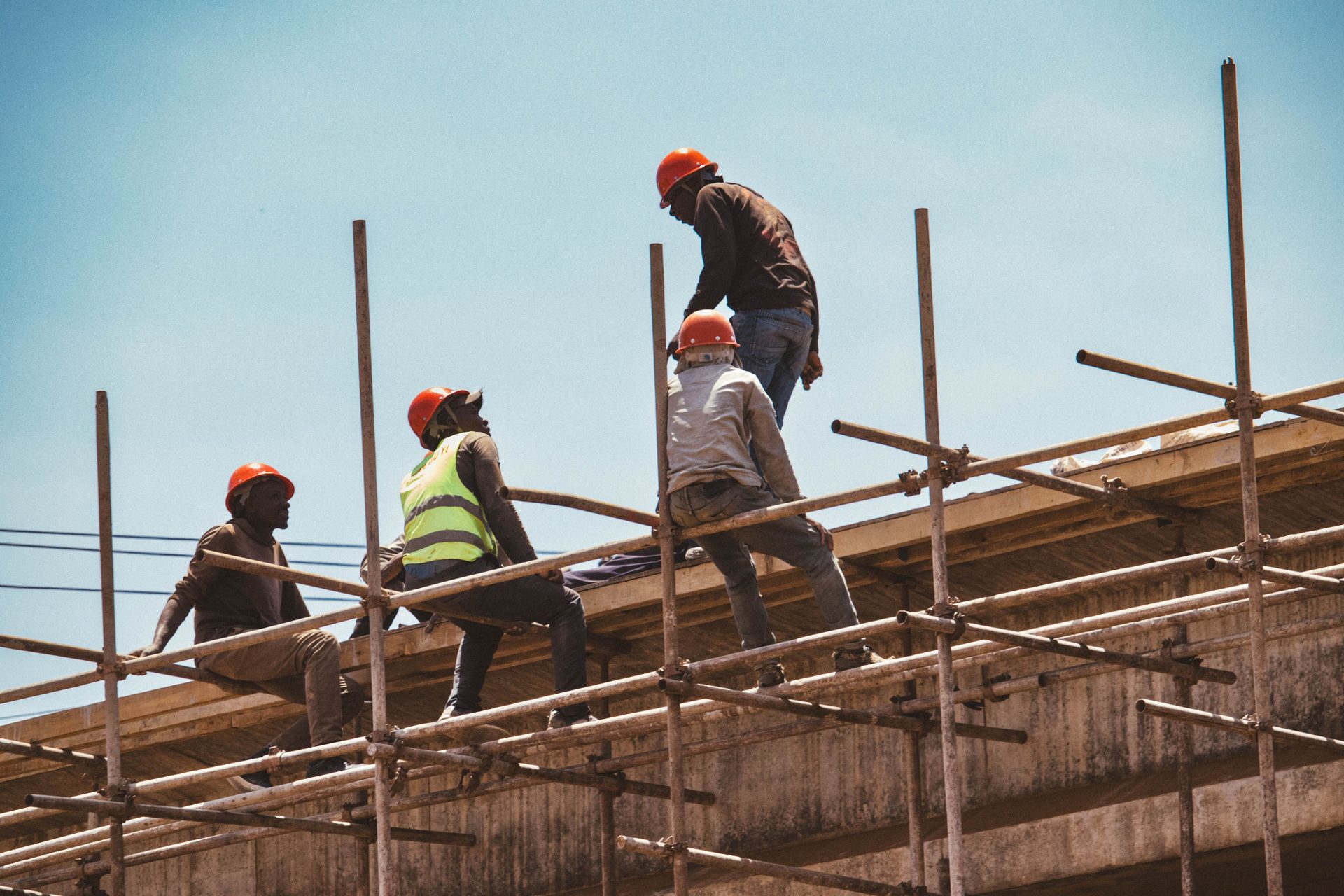 Construction workers in hard hats on scaffolding against a bright sky